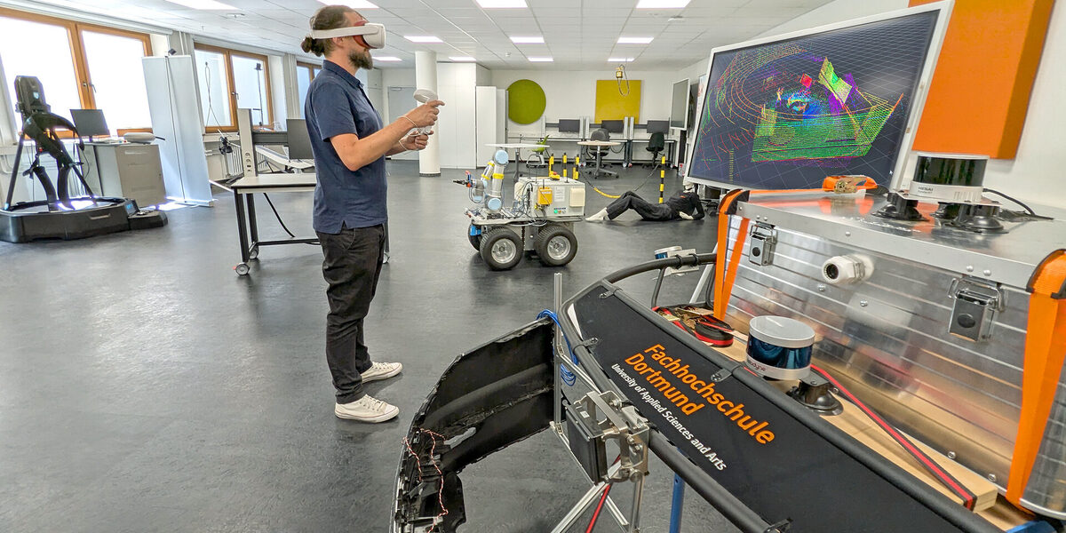 A person wearing VR goggles stands in a laboratory. In front of her is a monitor with colorful lines.