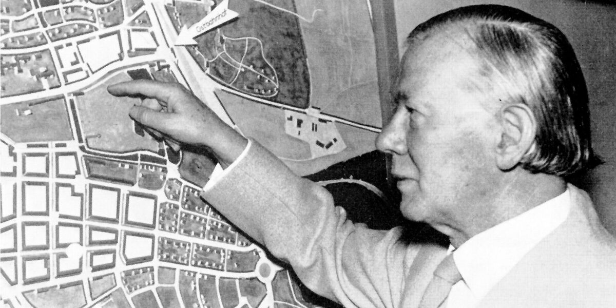 A male person stands in front of a city map and points to a square.