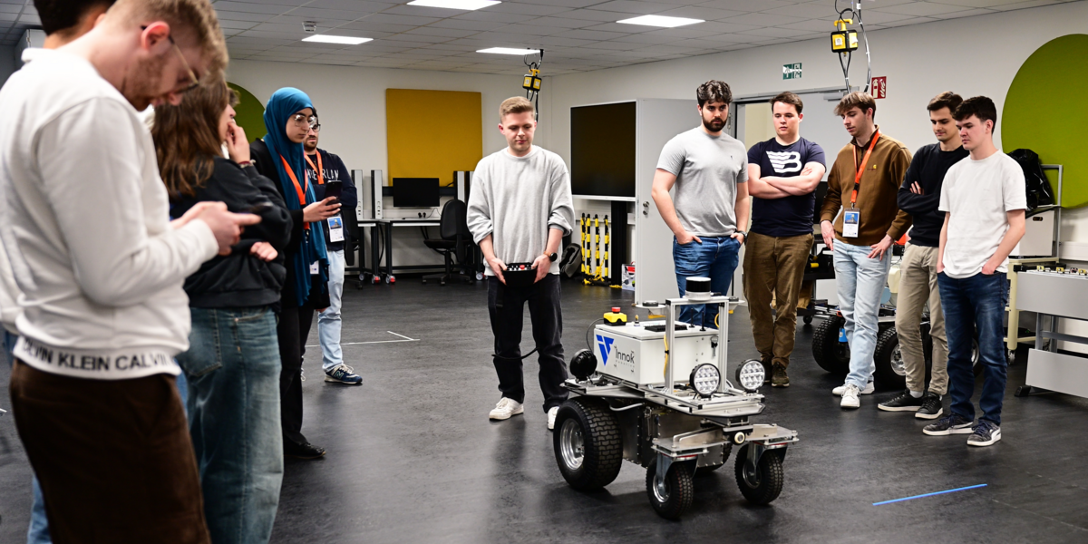 Eine Gruppe Studierende steht um einen mobilen Roboter in einem Labor, um ein entwickeltes Fahrassistenzsystemen zu testen.