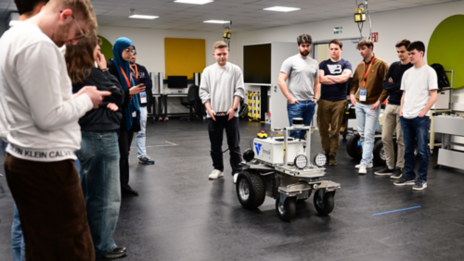 Eine Gruppe Studierender steht um einen mobilen Roboter in einem Labor, um ein Fahrassistenz-System zu testen.