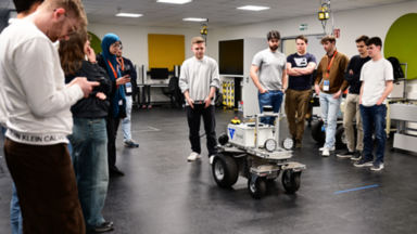 Eine Gruppe Studierender steht um einen mobilen Roboter in einem Labor, um ein Fahrassistenz-System zu testen.
