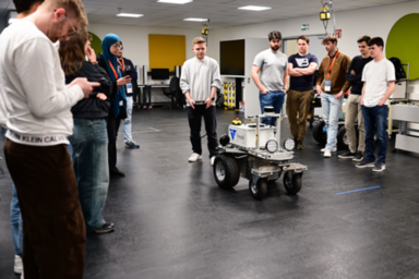 Eine Gruppe Studierender steht um einen mobilen Roboter in einem Labor, um ein Fahrassistenz-System zu testen.