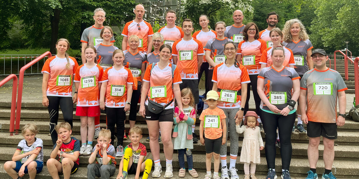 Eine Gruppe von Menschen steht in mehreren Reihen auf einer Treppe, alle tragen Laufshirts der FH Dortmund und schauen zur Kamera.