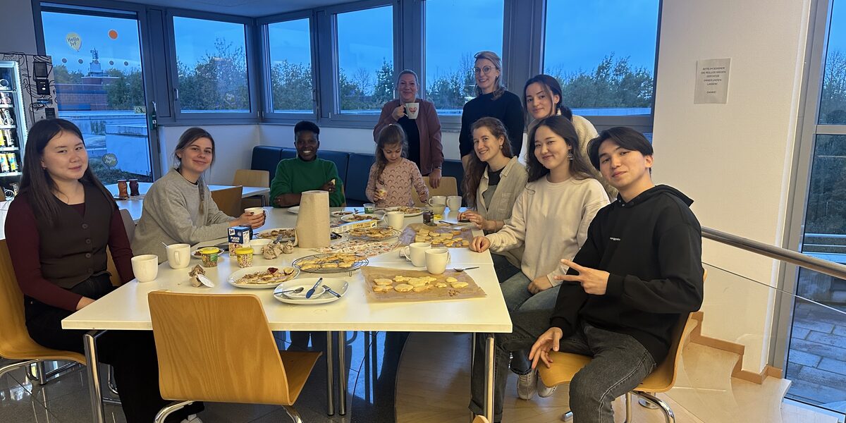 Mehrere Personen sitzen an einem Tisch mit Keksen und Kaffe.