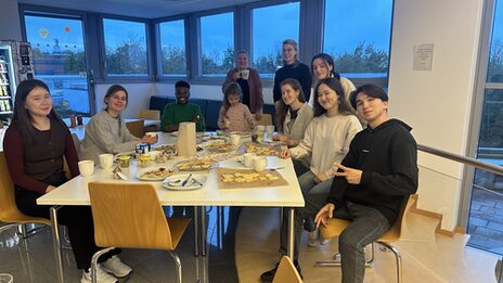 Mehrere Personen sitzen an einem Tisch mit Keksen und Kaffe.