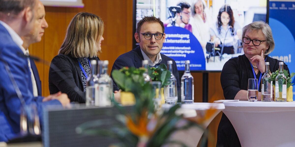 Vier Personen sitzen auf einer Bühne und sprechen miteinander in einer Diskussionsrunde.