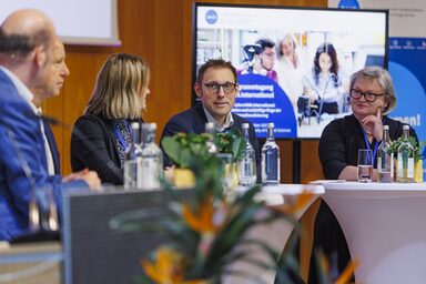 Vier Personen sitzen auf einer Bühne und sprechen miteinander in einer Diskussionsrunde.