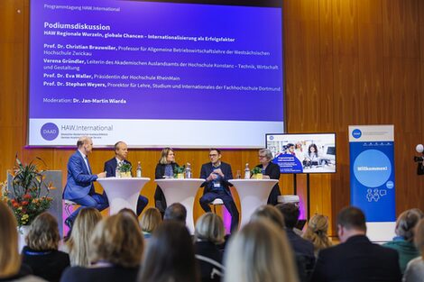 Vier Personen sitzen auf einer Bühne und sprechen miteinander in einer Diskussionsrunde.