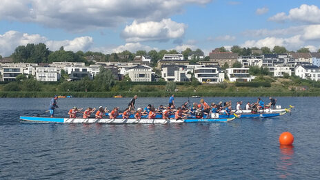 There are several boats on a lake, each with many paddlers.