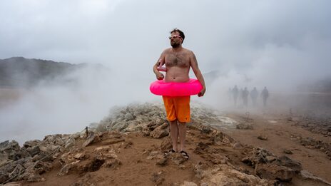 Auf dem Bild ist ein Mitglied des MSG-Kollektivs in einem natürlichen Pool in Island zu sehen. Das Bild ist inszeniert, u.a. mit einem rosa Schwimmreifen