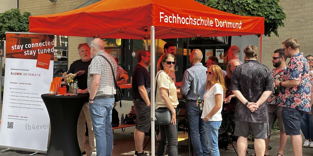 Absolvent*innen stehen am Alumni-Stand des Fachbereichs und unterhalten sich.