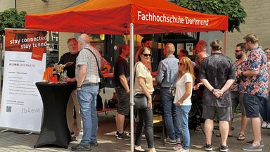 Absolvent*innen stehen am Alumni-Stand des Fachbereichs und unterhalten sich.