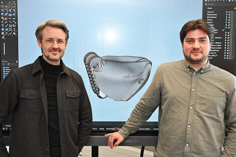 Zwei Personen stehen vor einem großen Bildschirm, auf dem ein 3D-Modell zu sehen ist.