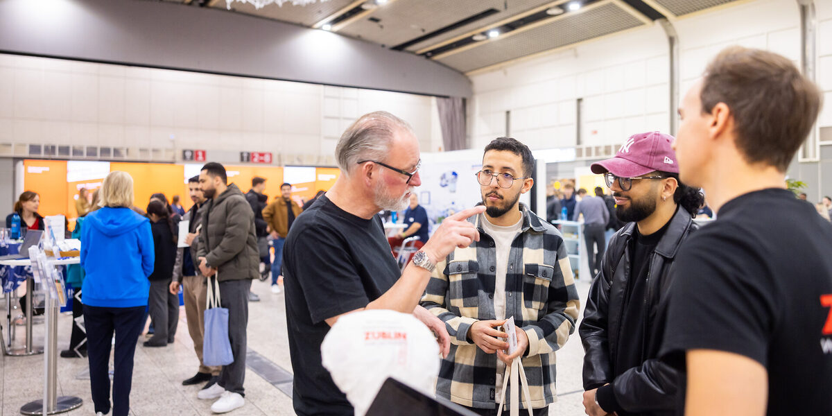 Mehrere Personen im Gespräch miteinander. Im Hintergrund sind weitere Messestände zu sehen.