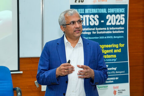 Eine Person spricht, im Hintergrund ist ein Roll-up der ISITSS-Konferenz zu sehen.