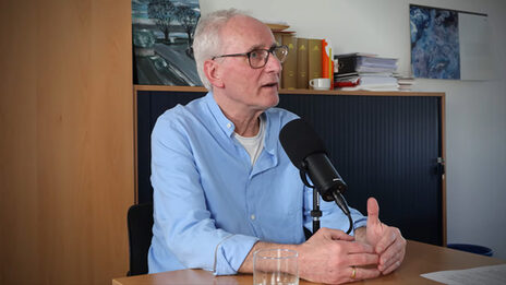 A person sits at a table in front of a microphone and speaks.