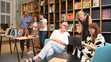 Zwei kleine Gruppen stehen in einer Bibliothek zusammen und diskutieren miteinander.