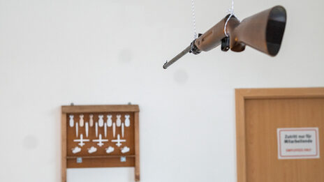 Room installation. A rifle attached to the ceiling is aimed at a small shooting range. The targets are in the shape of bombs and war missiles.