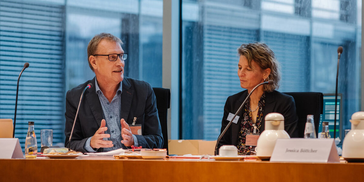 Two people sit next to each other at a table with microphones.