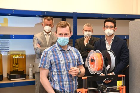 Several people stand around a 3D printer.