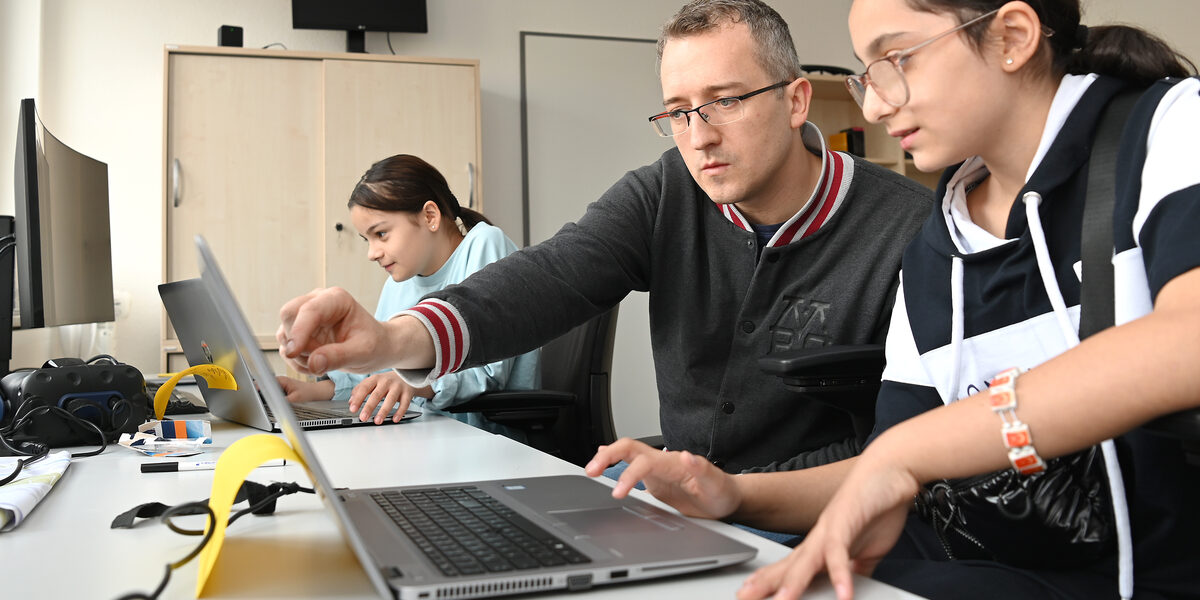 Drei Personen schauen auf Notebook-Monitore. Eine Person erklärt etwas.