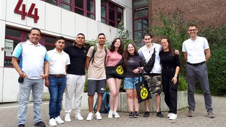 Nine people stand in front of the entrance to a university building.