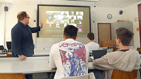 People sit in a seminar room and look at a screen on which other people are connected.