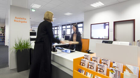Photo of a student handing a book to a female member of library staff at the service counter__Photo of a female student handing a book to a female member of library staff at the service counter