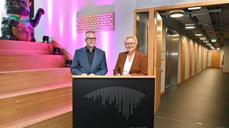 Two people stand at a desk in the foyer of the Academy for Theater and Digitality and sign a contract.