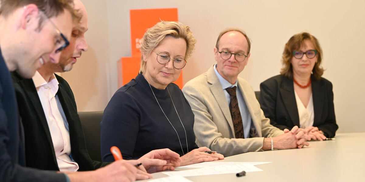 Mehreren Personen sitzen an einem Tisch, sie unterschreiben Papiere.