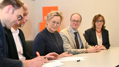 Mehreren Personen sitzen an einem Tisch, sie unterschreiben Papiere.