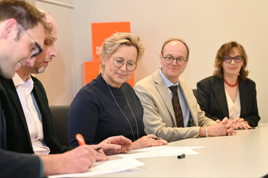 Mehreren Personen sitzen an einem Tisch, sie unterschreiben Papiere.