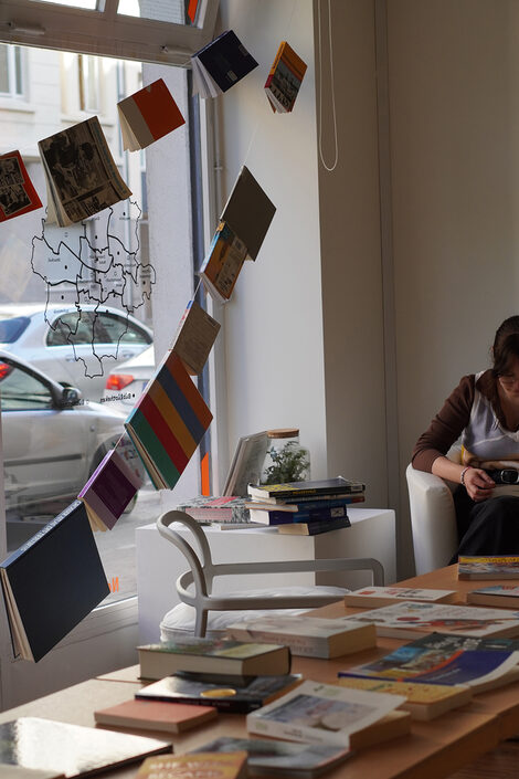 Bücher hängen verteilt auf einer Schnur, rechts sitzt eine Person und liest ein Buch.