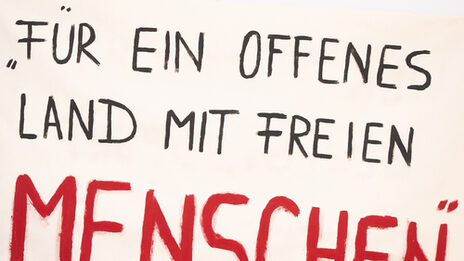 Plakat mit Aufschrift: Für ein offenes Land mit freien Menschen. Im Hintergrund andere im Bildanschnitt abgeschnittene Plakate mit Auschrift.