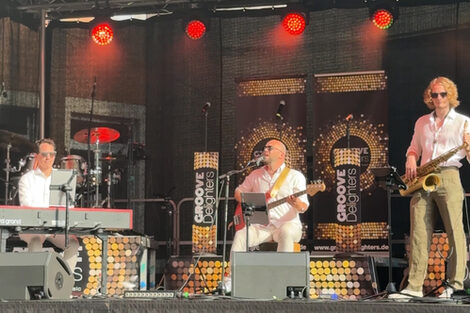 Drei Personen mit Keyboard, Bass und Saxofon auf einer Bühne.