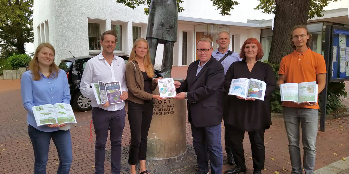 Eine Gruppe von Menschen steht vor einer Statue und präsentiert ein Buch.