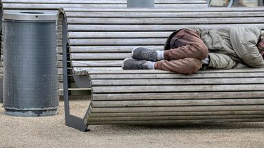 Eine wohnungslose Person liegt auf einer Bank