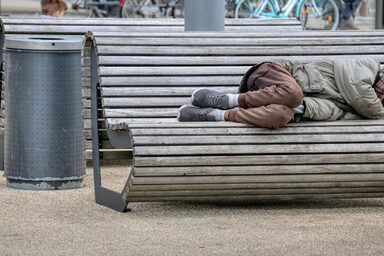 A homeless person lies on a bench