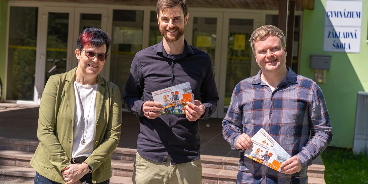 Drei Personen stehen vor einer Schule und halten Flyer der FH Dortmund in den Händen.