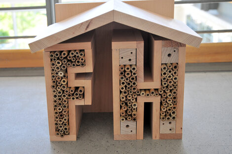 Insektenhotel aus Holz in Hausform mit den Buchstaben „F“ und „H“, gefüllt mit Röhrchen und Bohrlöchern als Nistplätze.