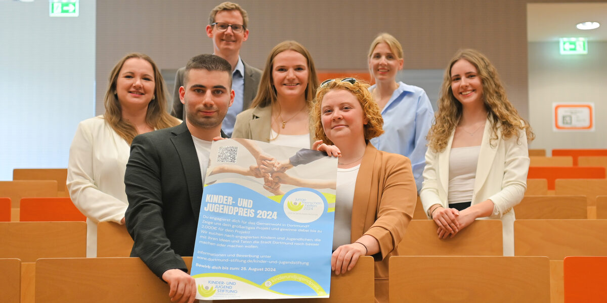 Several people are standing in the rows of seats in a lecture hall, the two at the front are holding a poster.