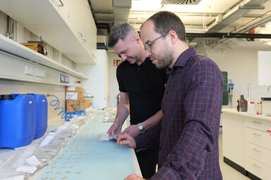 Two people are standing in a laboratory analyzing samples.