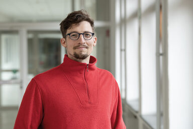Eine Person im roten Pullover schaut freundlich in die Kamera.