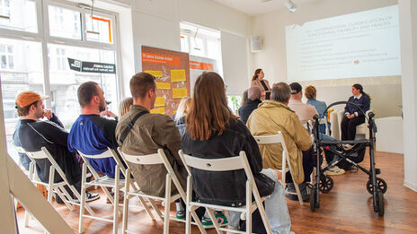 A presentation is beamed onto the wall. The audience looks forward.