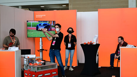 Exhibition stand with robots as exhibits; TV shows videos; stand employee holds up EduRob