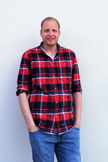 Male scholarship holder stands smiling in front of a white wall.