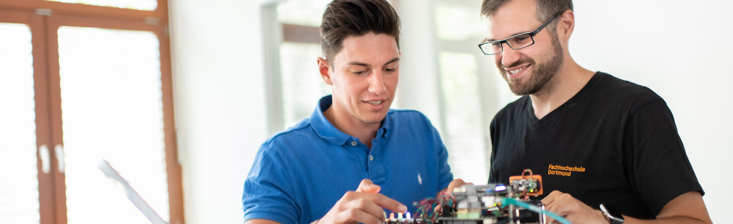 Photo of a student and an employee of the Laboratory for Energy Automation and Grid Management. They are standing next to each other and working on an electronic test setup.