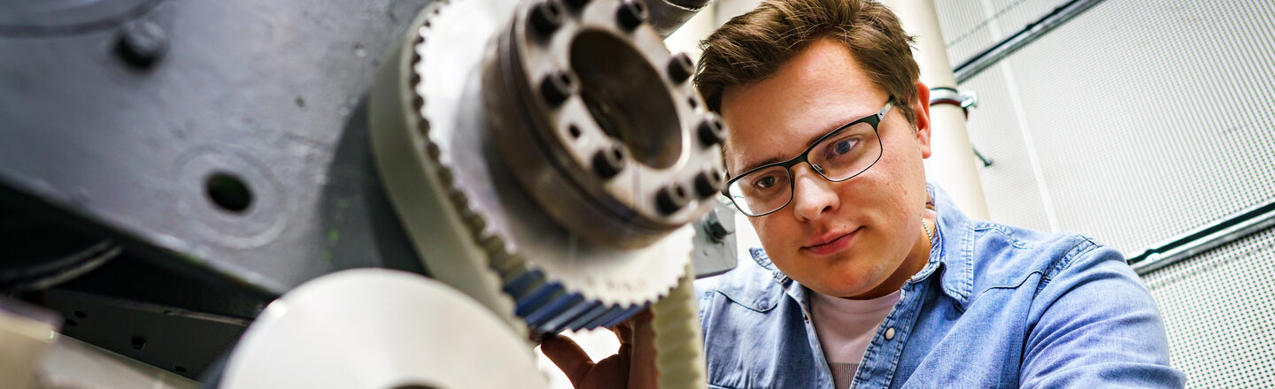 Photo of a young man adjusting something on an engine block.