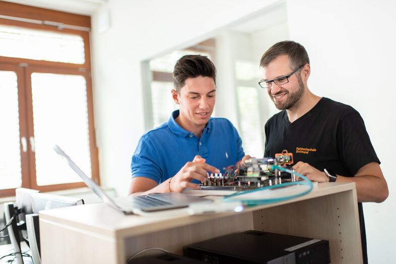 Foto eines Studenten und eines Mitarbeiters des Labors für Energieautomation und Netzführung. Sie stehen nebeneinander und arbeiten an einem elektronischen Versuchsaufbau.