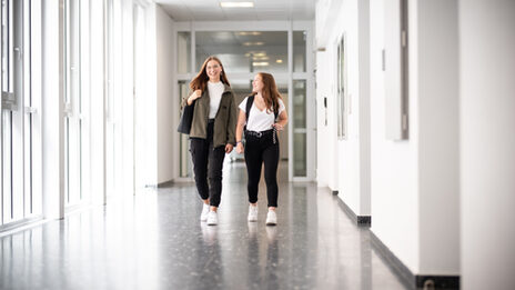 Photo of two girls running down the hallway laughing. __ Two girls run down the hallway laughing.